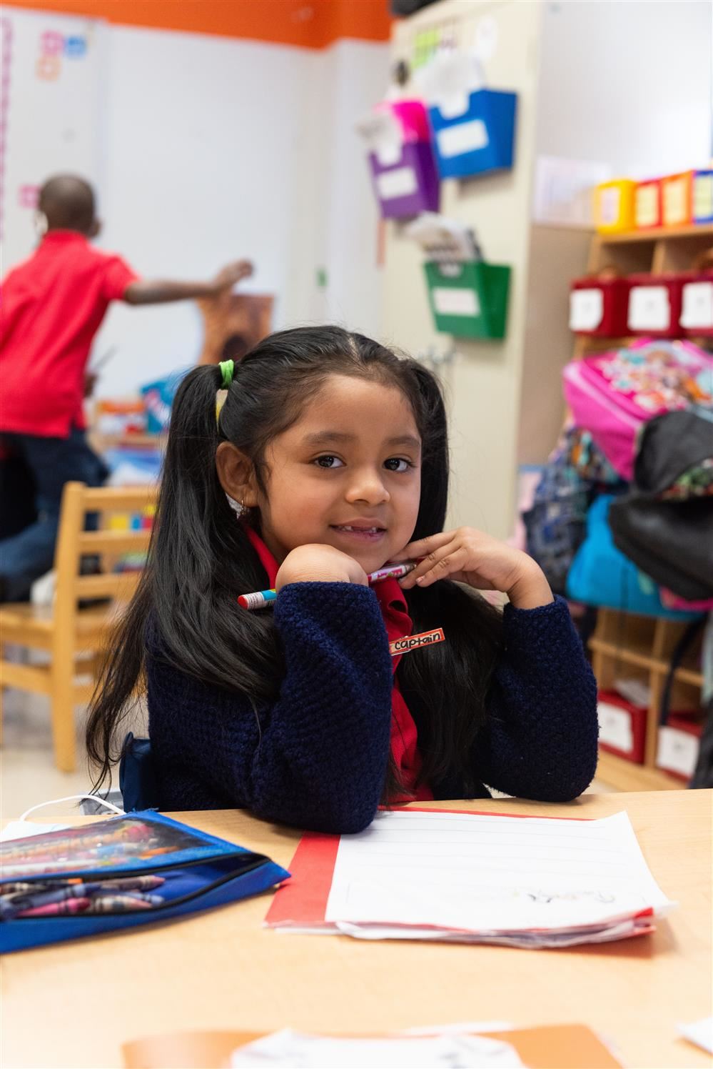 Student smiles while holding a pencil at a workstation